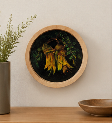 Round framed painting of flowers on a wall above a wooden shelf with a plant and bowl.
